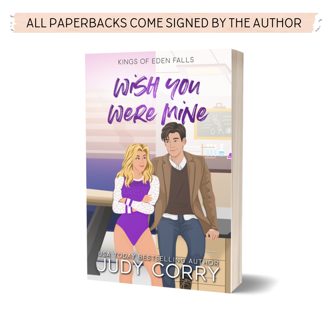 Paperback cover of 'Wish You Were Mine' by Judy Corry with an illustrated couple. The woman is wearing a gymnastics leotard and the man is wearing a sport coat and sweater vest. The background is split in two. One side shows a gymnastics facility and the other side shows a chemistry lab.