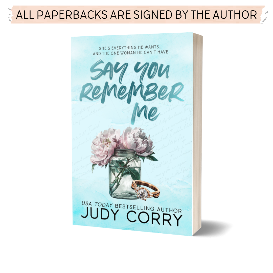 Paperback book cover for 'Say You Remember Me' by Judy Corry, featuring a vase with flowers on the front, an engagement ring, and the author's name.